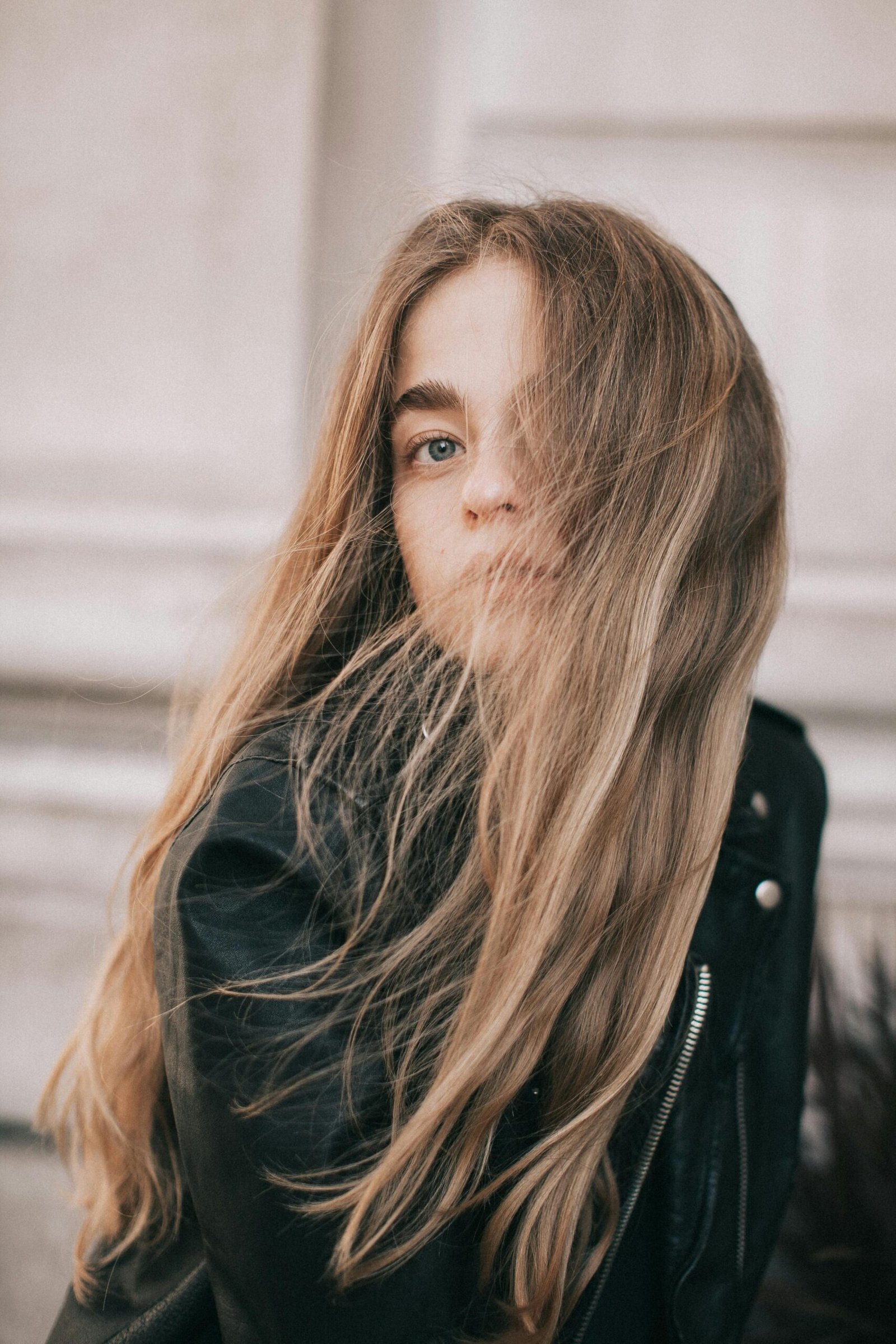 Portrait of a young woman with long hair in the wind, wearing a leather jacket outdoors.